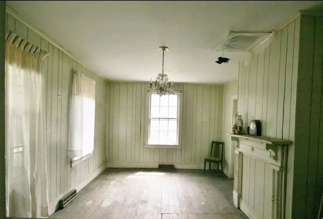 Living room with wood paneling and worn floorboards before renovation