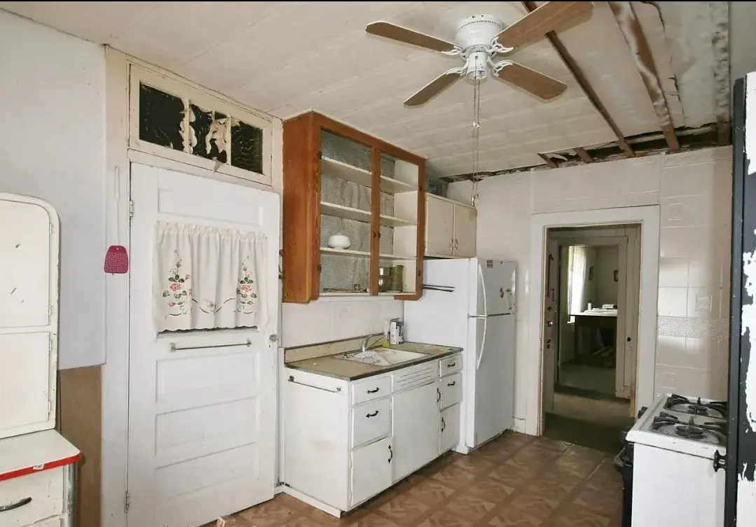 Outdated kitchen before remodel with old cabinets, ceiling fan and damaged ceiling