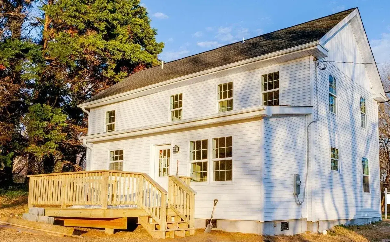 Back of the renovated house with new white siding and wood deck with stairs