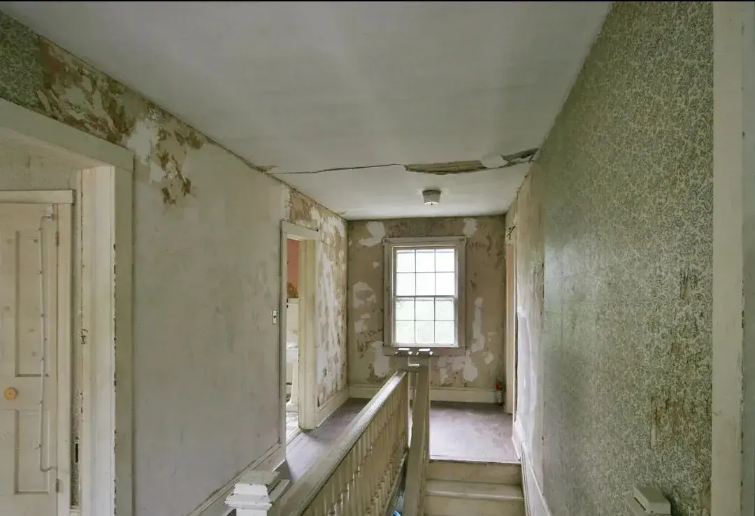Upstairs hallway with peeling wallpaper and damaged plaster before renovation