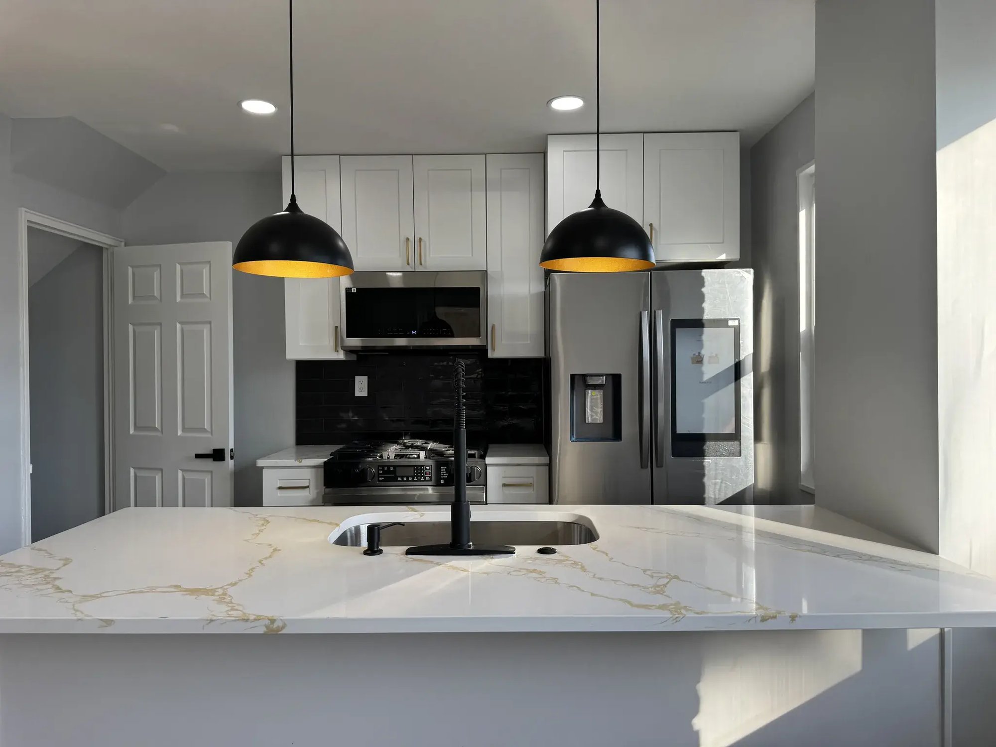 New kitchen with white shaker cabinets, quartz island and black pendant lights