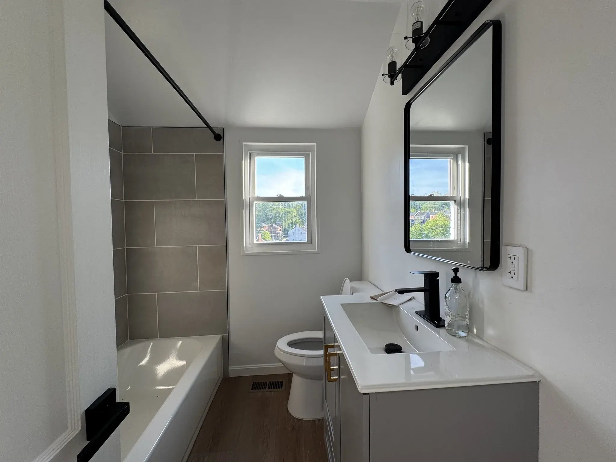 Renovated bathroom with gray tile, white vanity and black mirror