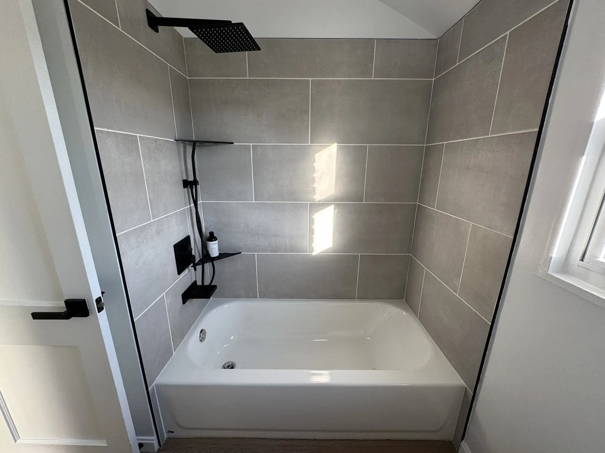 Tub with large gray tile surround and matte black shower fixtures