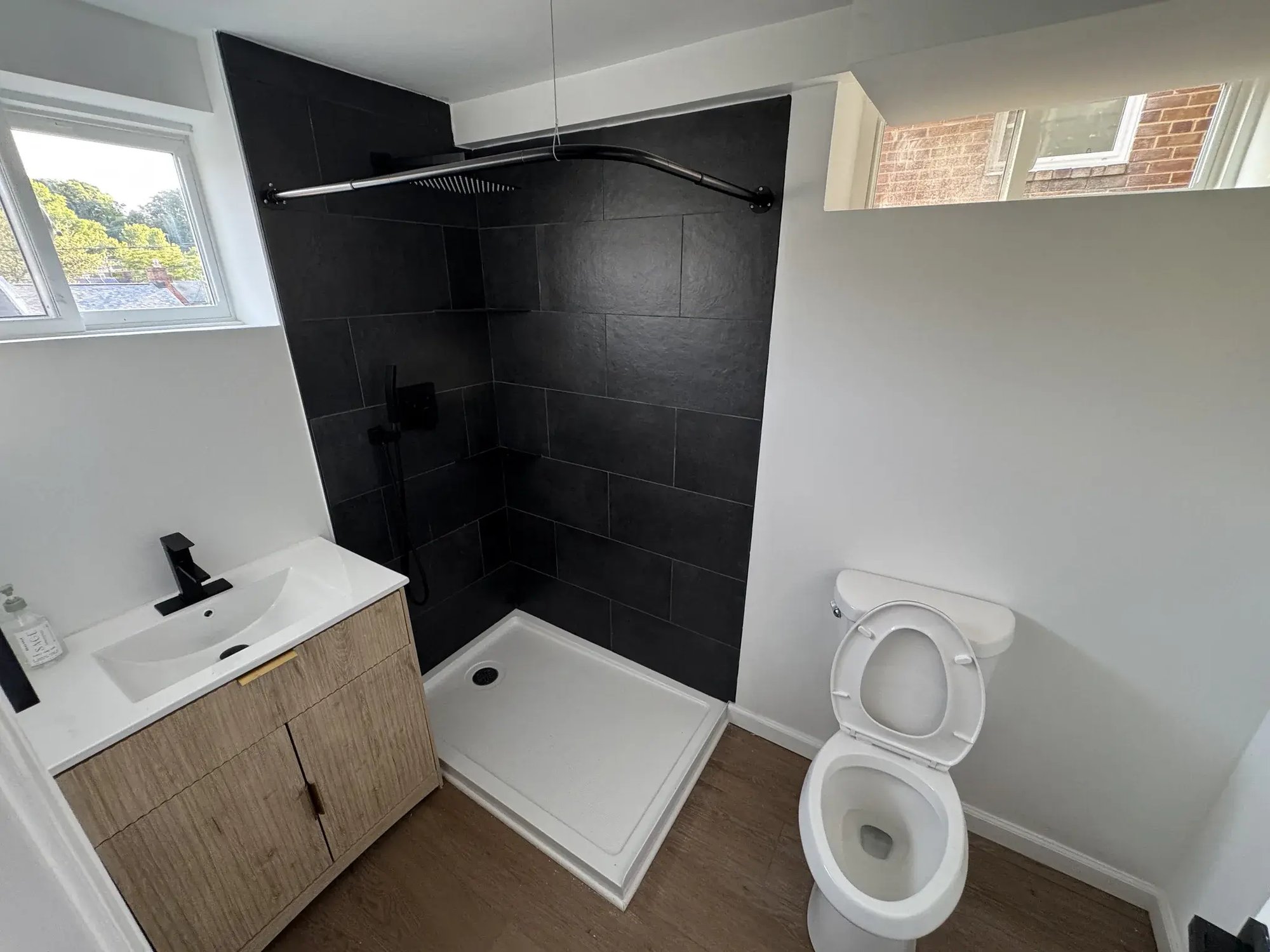 Bathroom with black tile shower wall and wood vanity