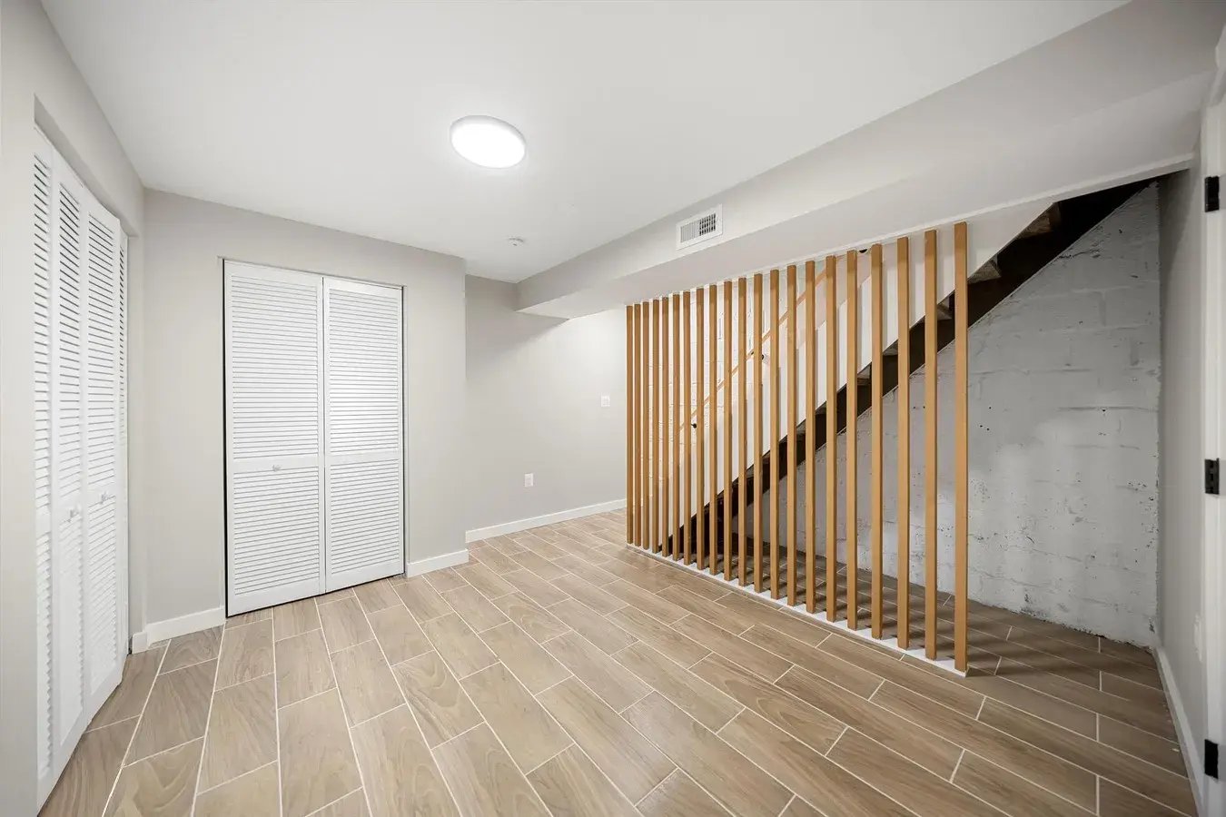 Finished basement with wood slat stair screen and louvered closet doors