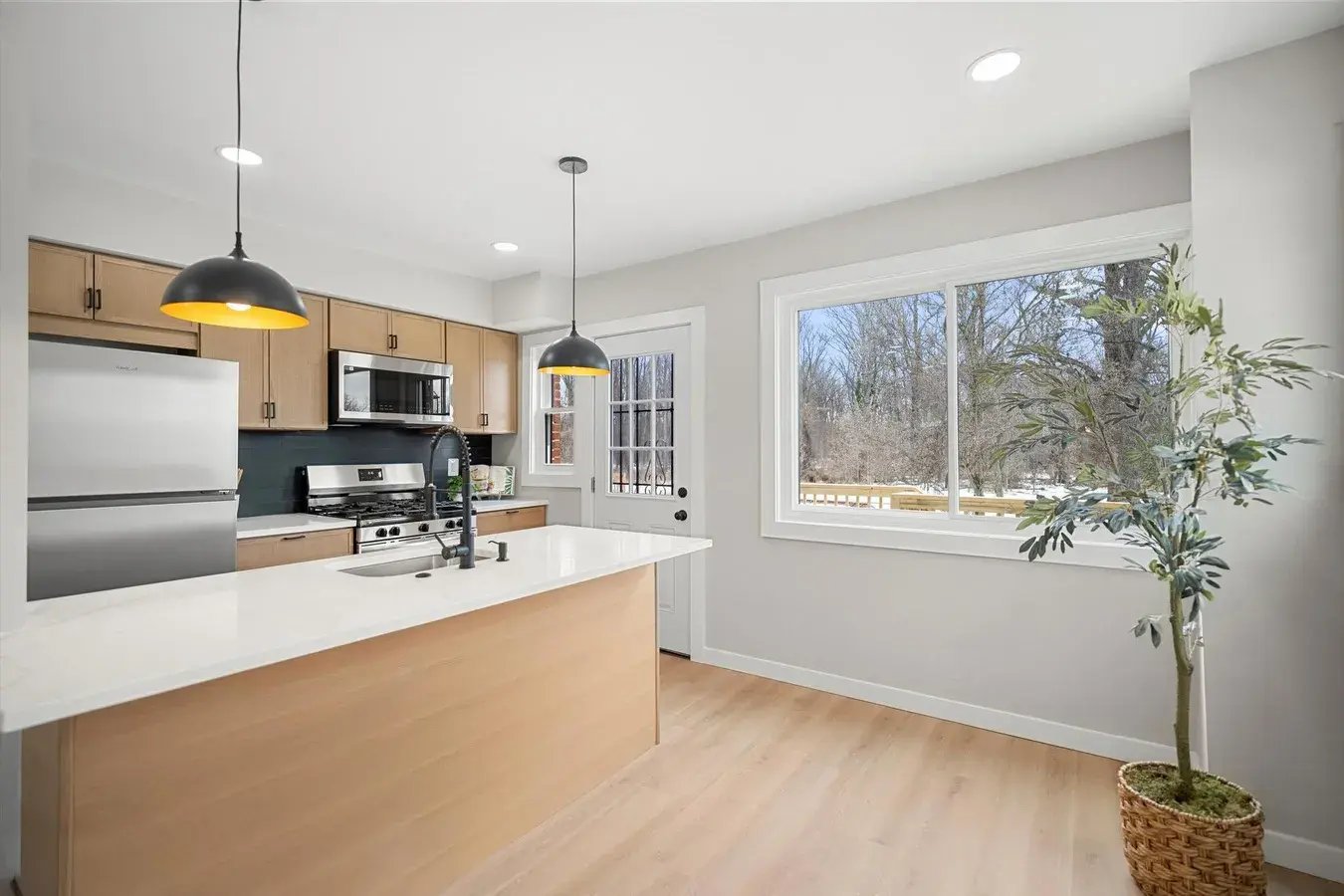 Renovated kitchen with quartz island, light wood cabinets and a garden view window